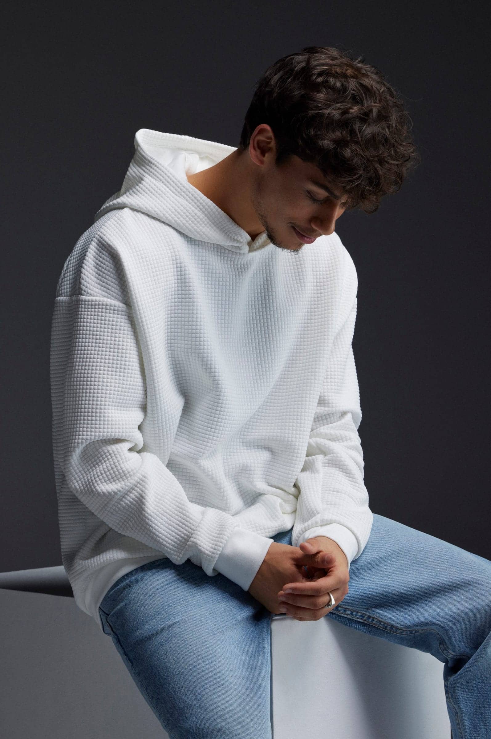 Harris J in a white quilted hoodie, seated and looking down with a smile