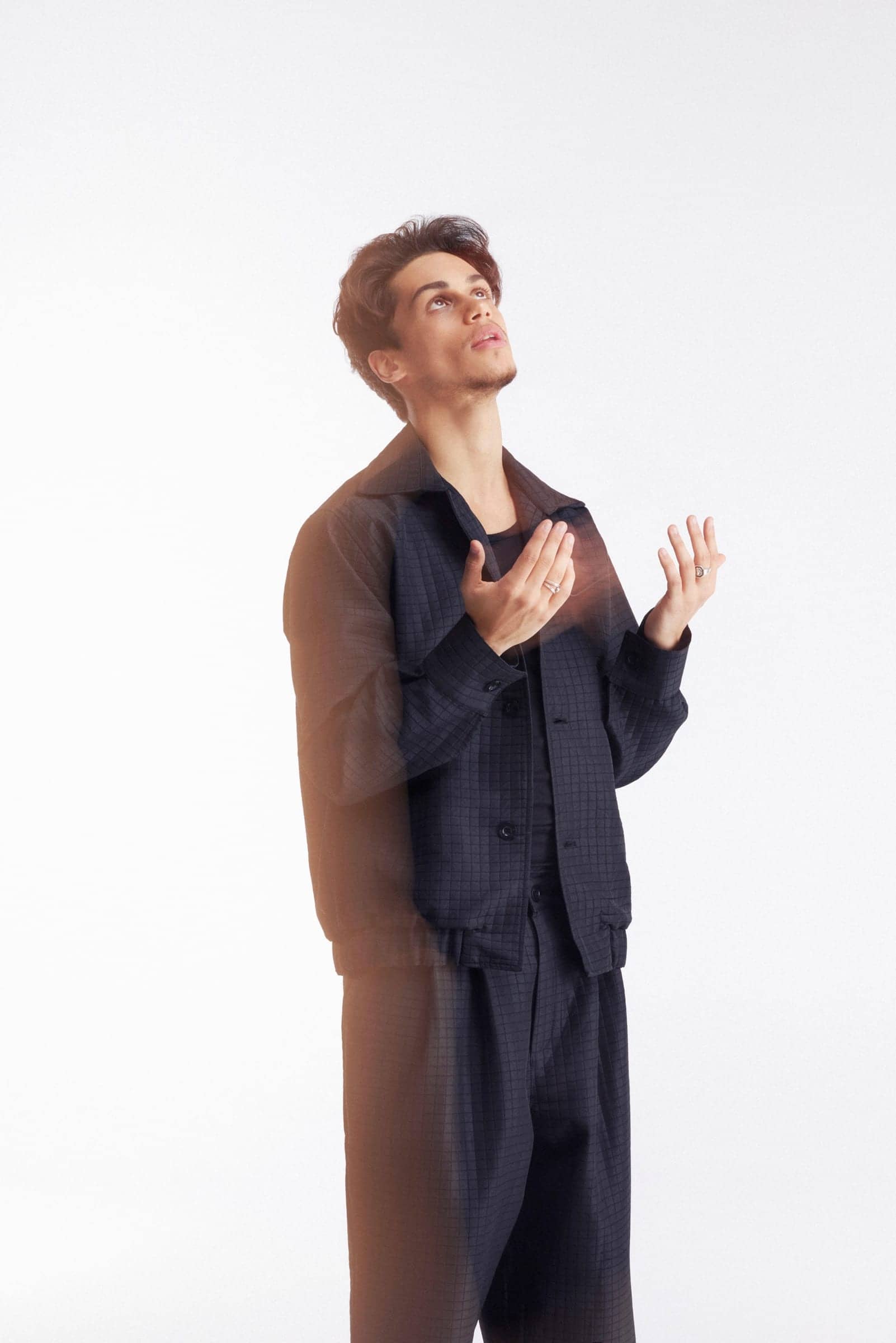Harris J looking upwards with palms raised, against a white backdrop