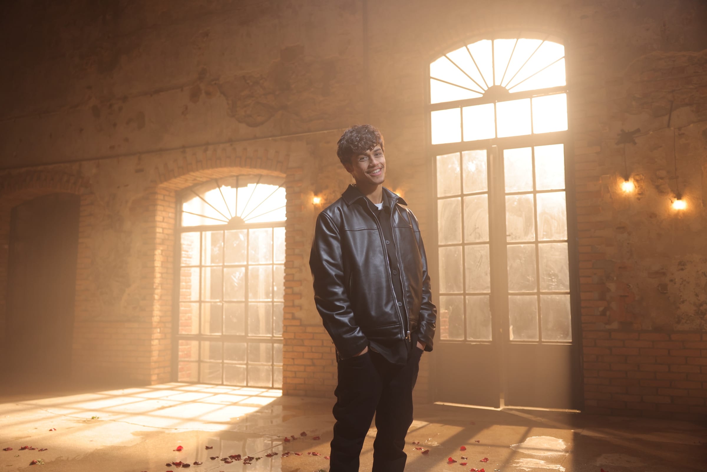 Harris J smiling in a leather jacket in front of arched sunlit windows
