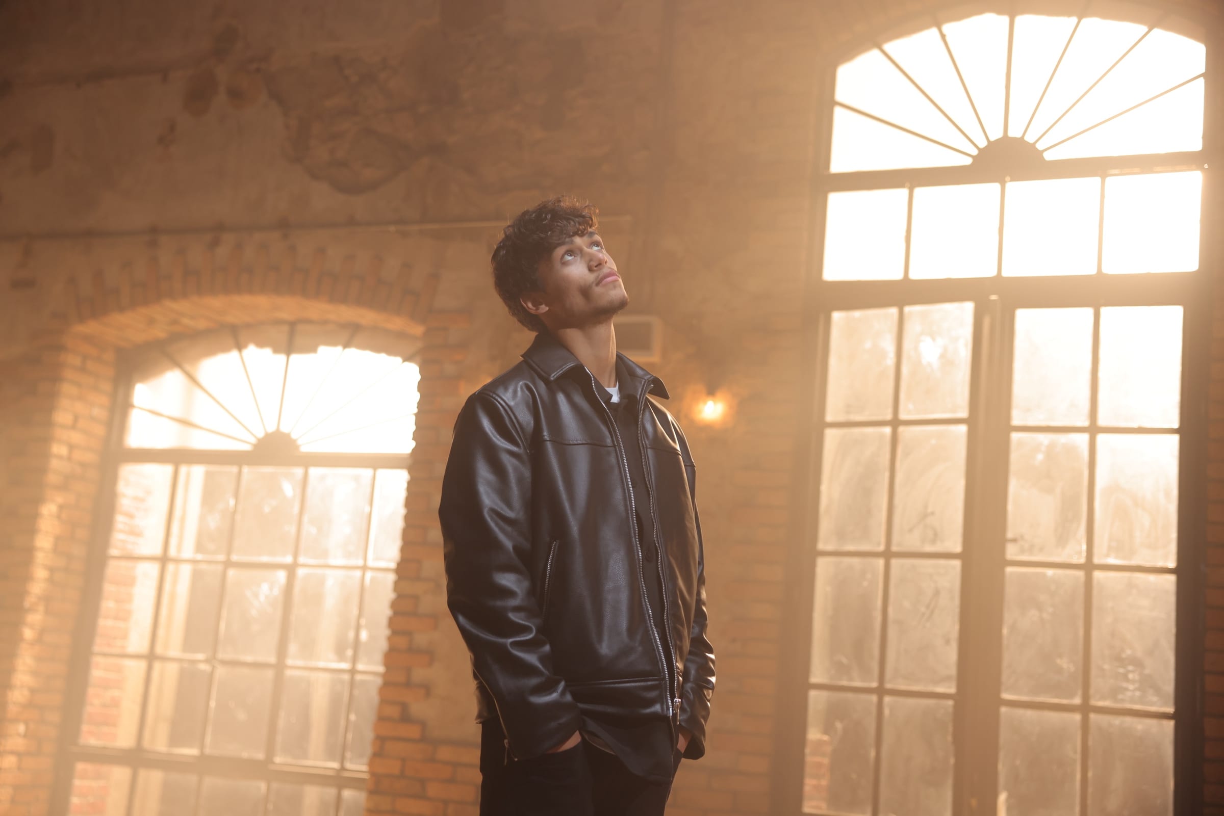 Harris J looking upwards in a hall of tall arched windows, lit by warm light