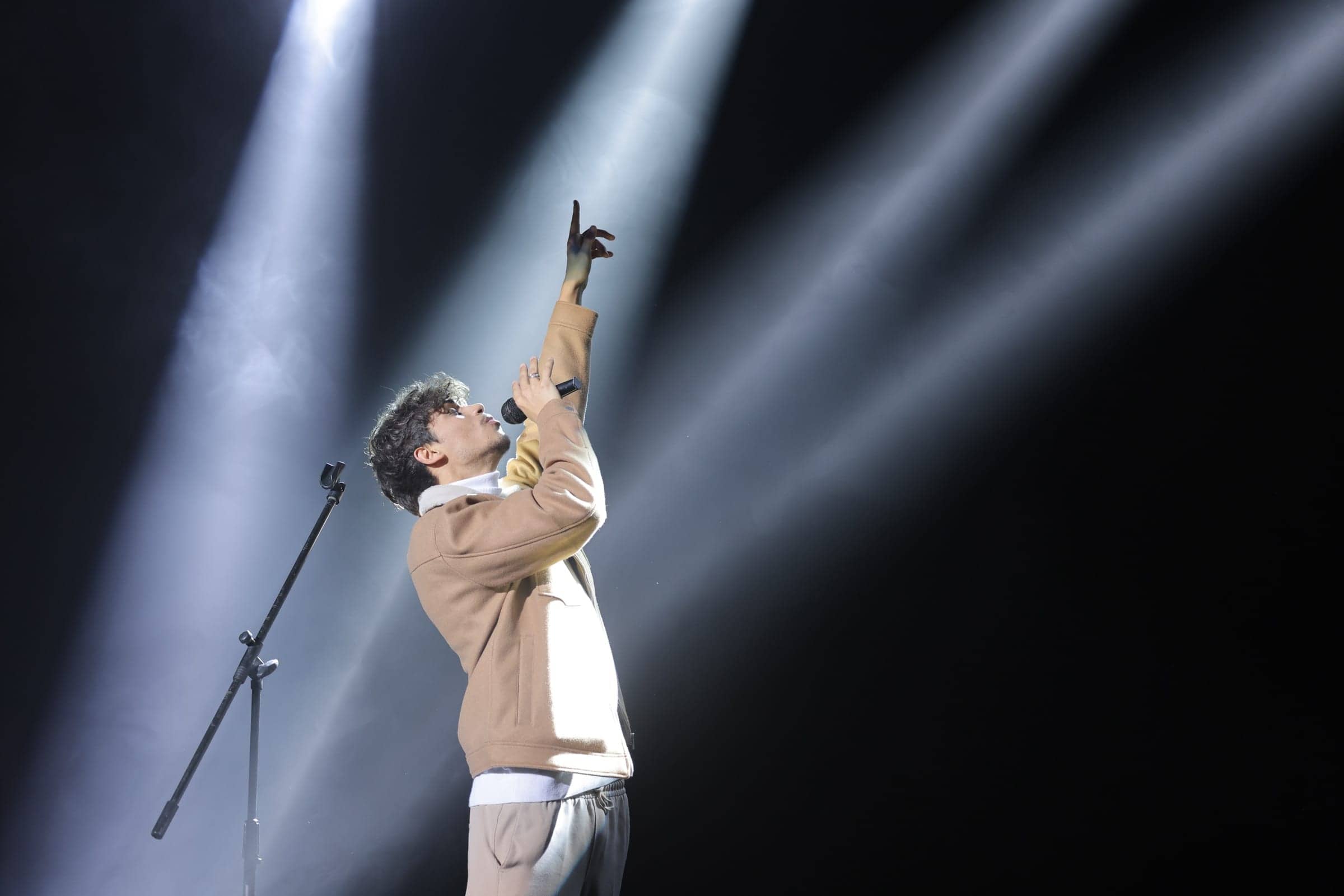 Harris J on stage, microphone in hand, pointing upwards through beams of light