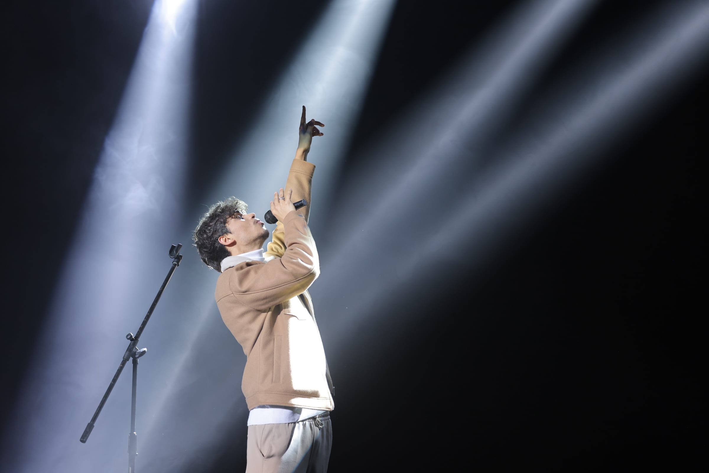 Harris J on stage, microphone in hand, pointing upwards through beams of white light